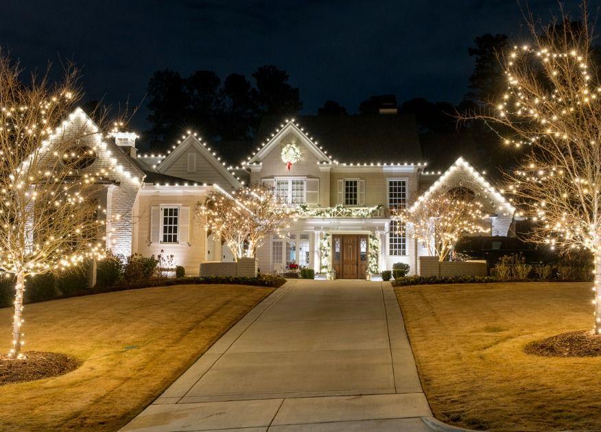 Elegant house with Christmas lights and decorations, including a wreath on the front door and illuminated trees.