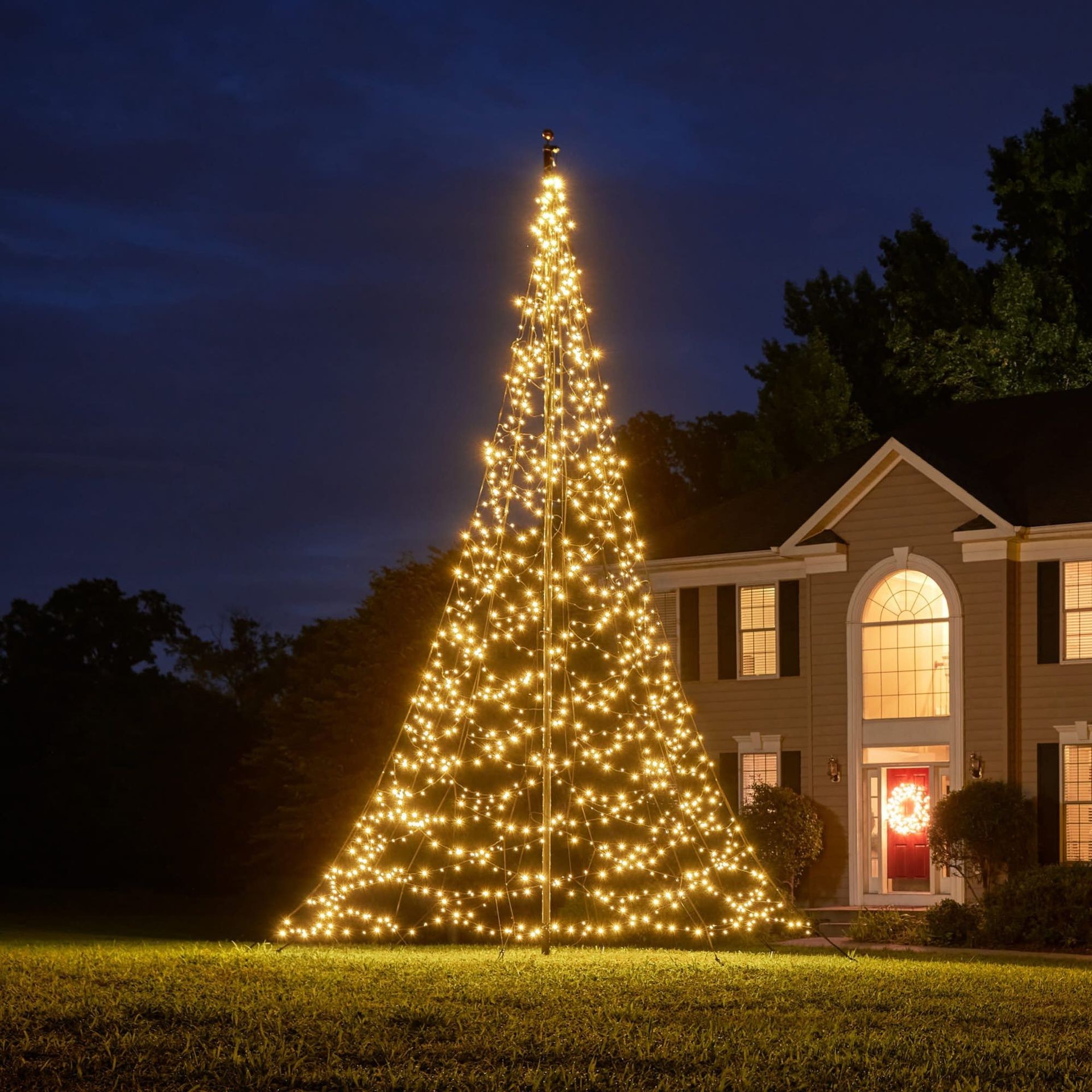 A house with golden Christmas lights shaped like a tree in the front yard, illuminated at night.